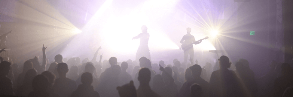Small music venue, a band are on stage in front of an audience, all in silhouette against purple lighting.